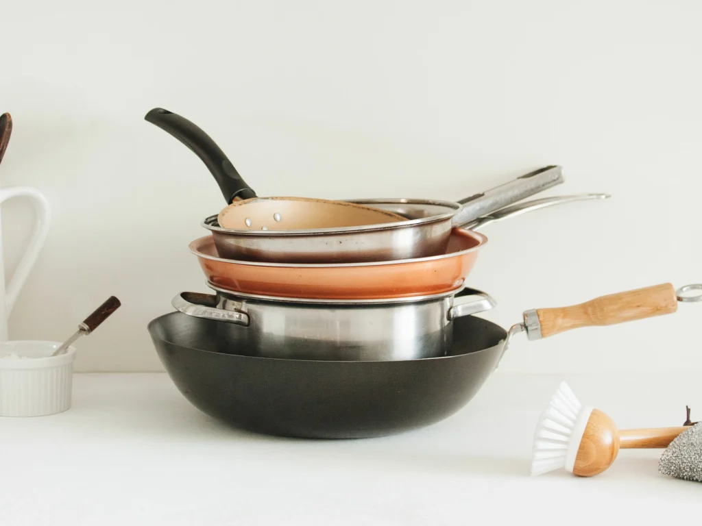 Stacked cookware, including non-stick pans, showing improper storage that may damage the coating.